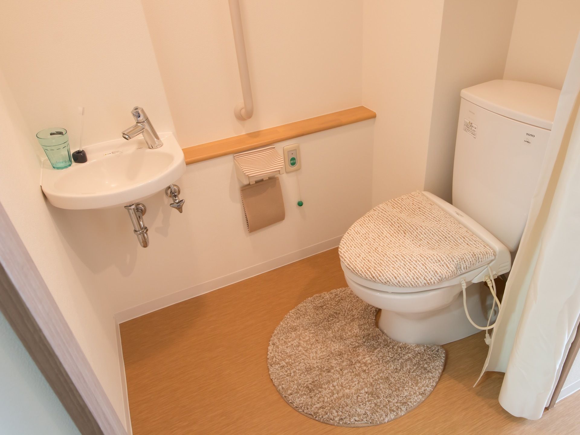 居室内にあるトイレは扉ではなくカーテンで仕切られている。温水洗浄便座を取りつけ、便座カバーがされている。