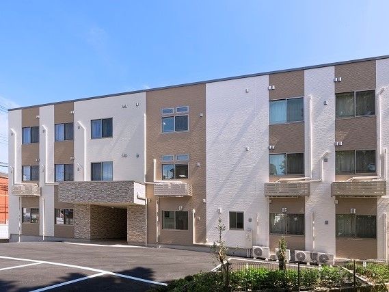 3階建ての建物はベージュの外壁にブラウンの縦じまが入ったモダンな外観。