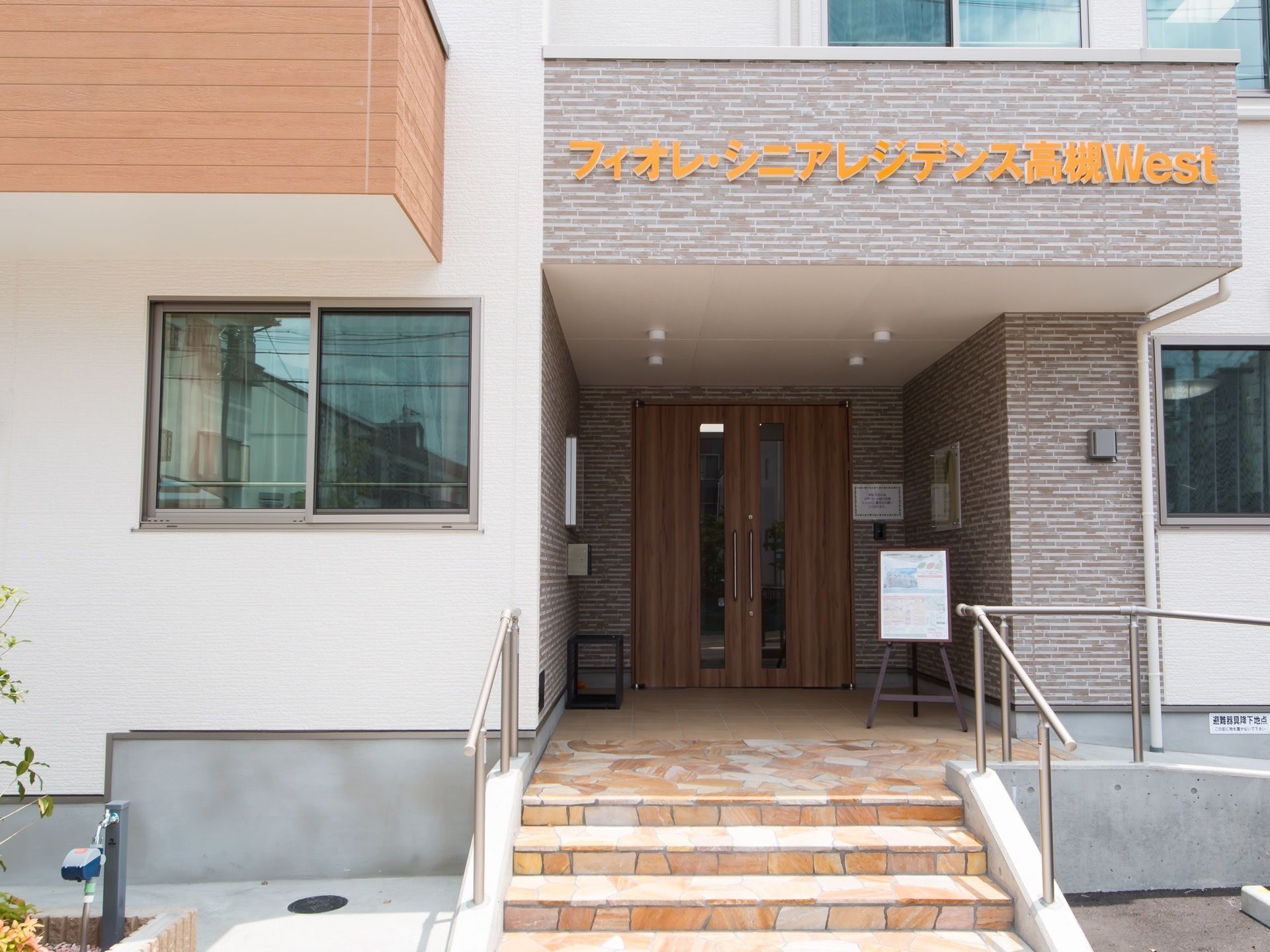 玄関の上には屋根が張り出しており、下向きの照明がある。また前面には看板代わりに施設名が取り付けられている。