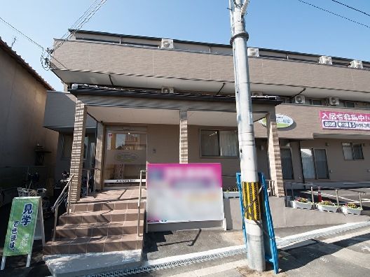 施設の玄関に続く階段の脇には、施設の料金案内の看板が設置されている。施設はブラウン色が基調の外壁になっている。