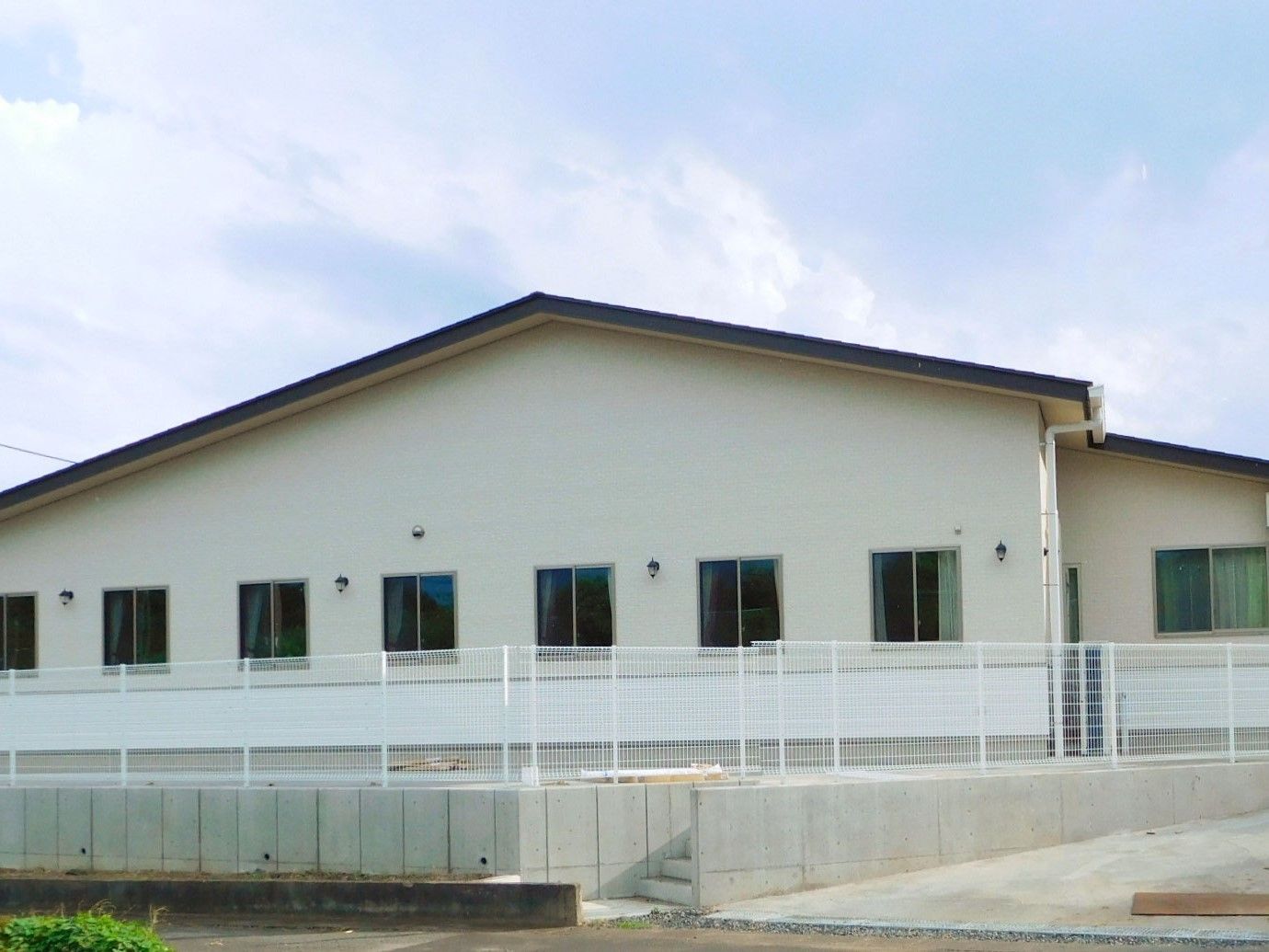 白い外壁の平屋建ての建物。建物周辺にはフェンスがある。