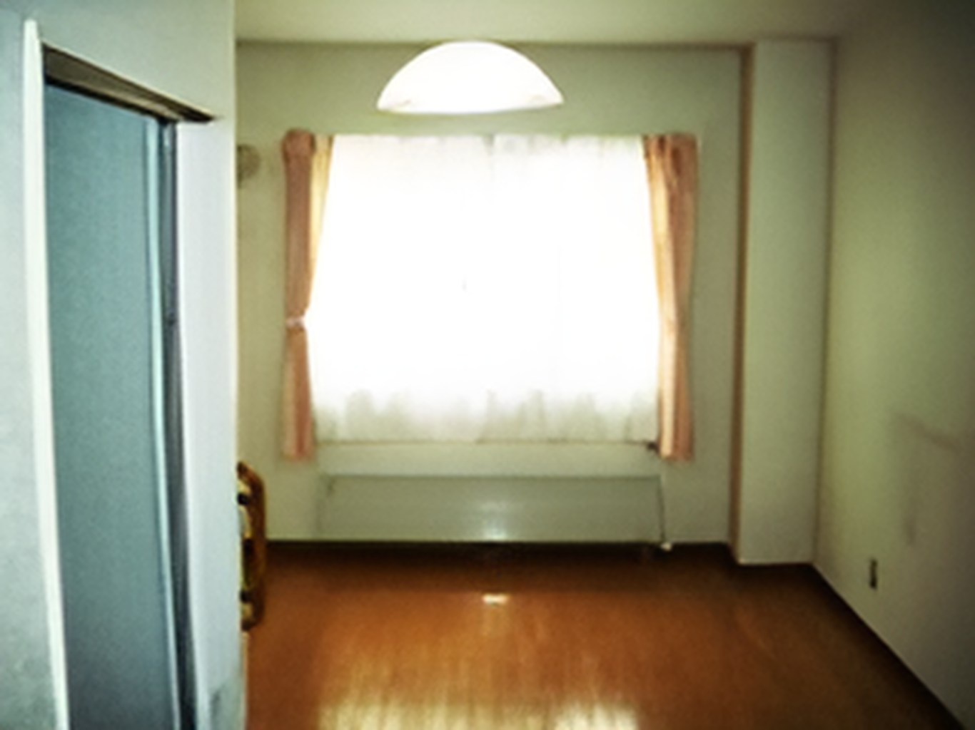 レースカーテンとカーテンがある大きな窓が付いているフローリングの部屋には家具や家電はない。