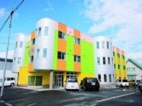 ライトグリーンやオレンジのアクセントが入ったカラフルな建物は3階建てで敷地内には駐車場がある。