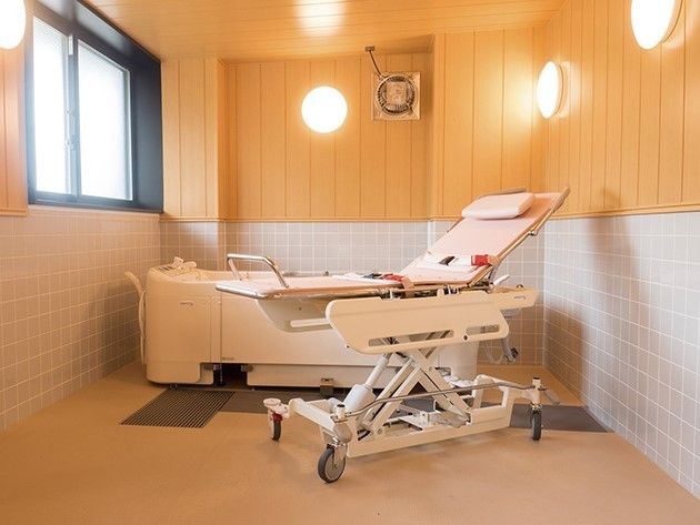 寝台浴が設置された浴室。下半分がタイル張り、上半分が木目調の壁となっていて明るい雰囲気。