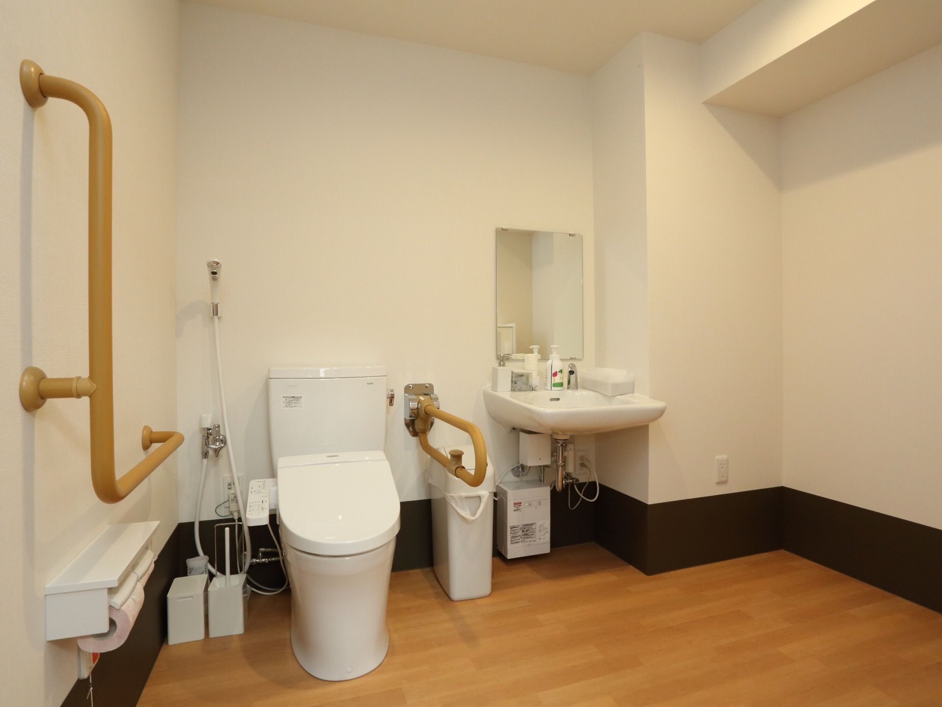 広々とした室内にはトイレのほかに洗面台とシャワーが設置されている。手すりが両サイドについている。ゴミ箱や掃除用具が置かれている。