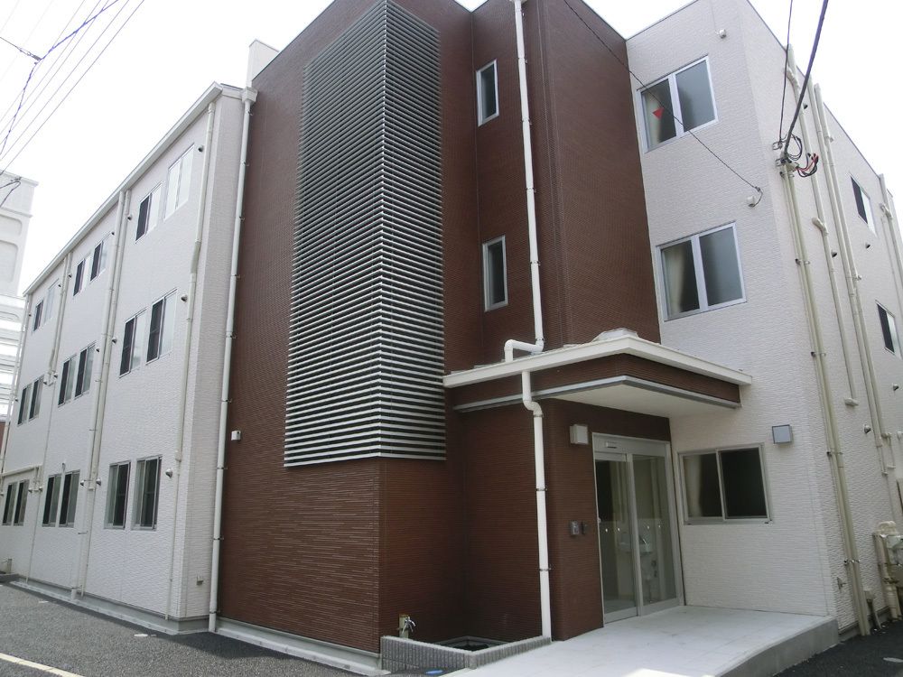 ブラウンと白の3階建ての建物にはたくさんの窓があり、玄関先には屋根が付いている。