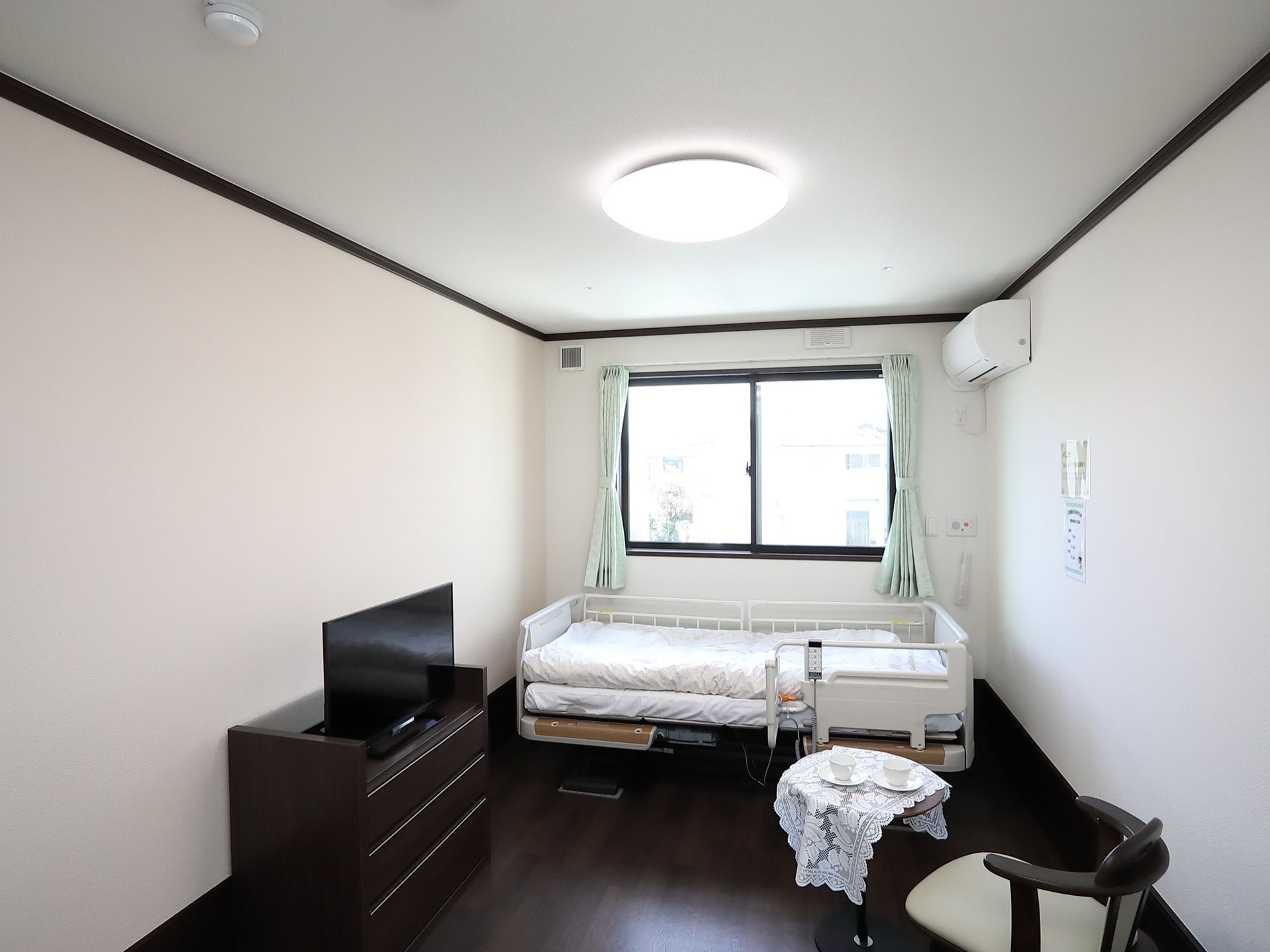 居室には転落防止柵がついた介護ベッドやエアコンが設置されている。小さな丸テーブルにはクロスがかけられている。