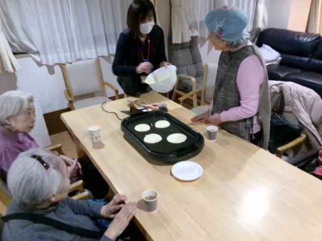 車いすの高齢男性のそばにはピンクのエプロンを付けた若い女性スタッフがいて、後ろには福祉車両がある。