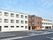 ３階建ての白い建物は玄関周りだけブラウン系。敷地が広く、駐車場も大きい。
