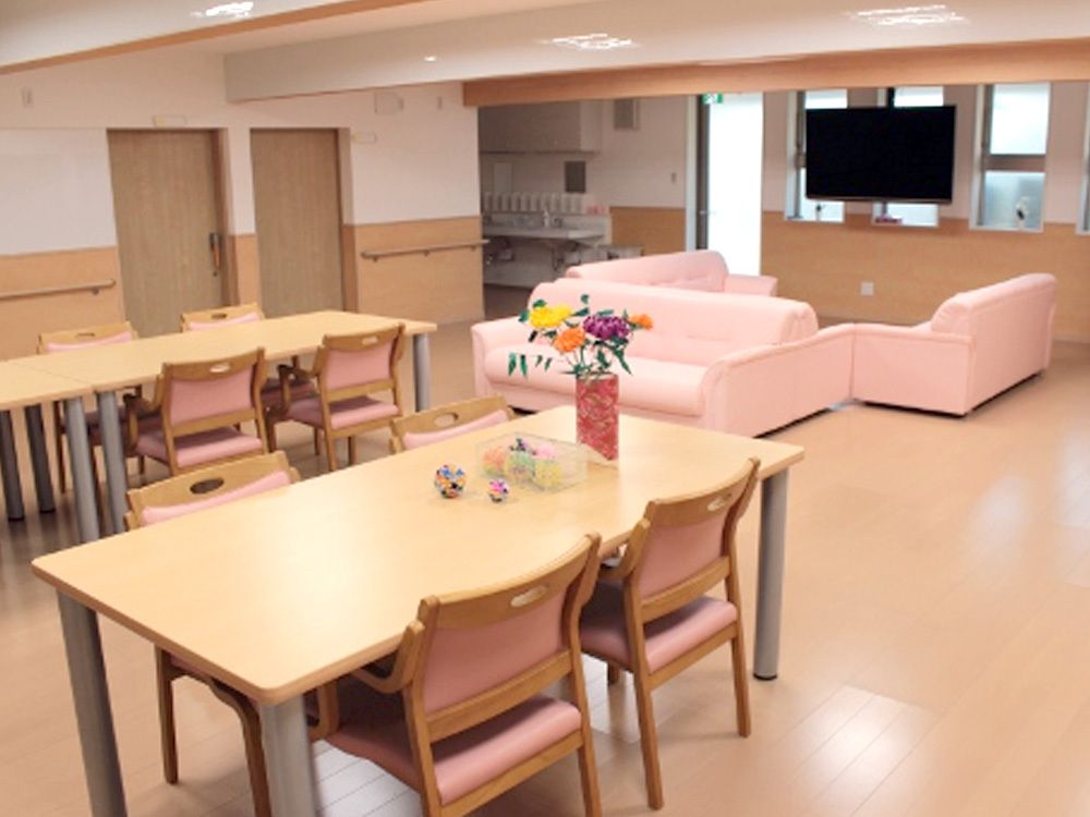 木製のダイニングテーブルが複数置かれ、テレビやソファもが設置されたリビングダイニング。