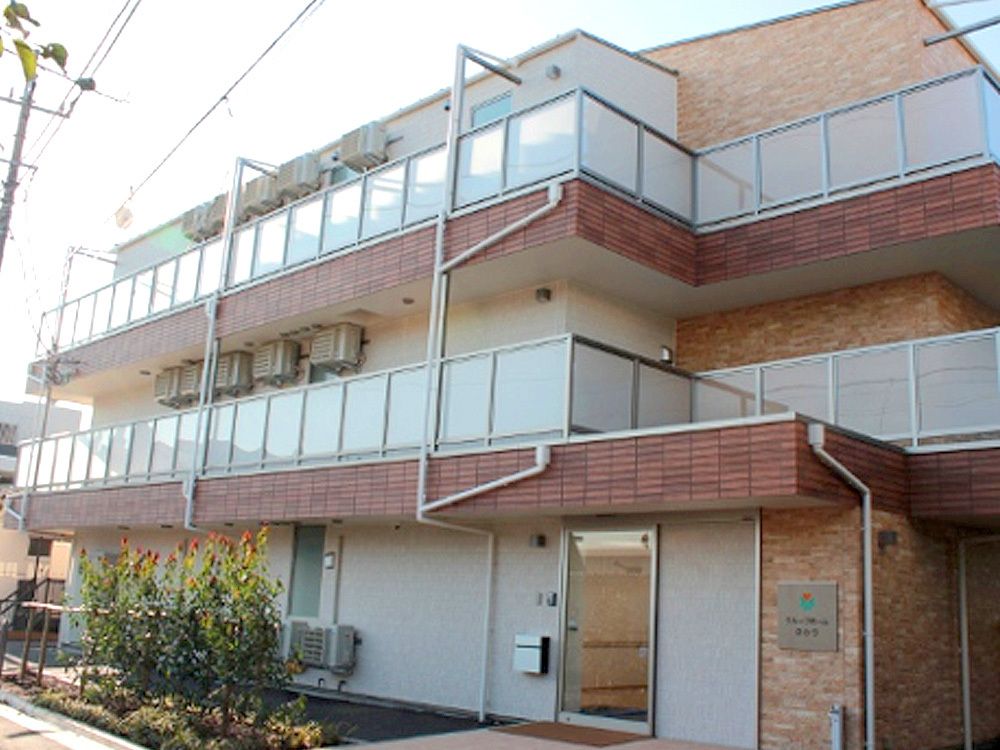 ブラウン系の外壁の３階建ての建物は日当たり良好。各フロアにベランダがあり、草木が植えられている。