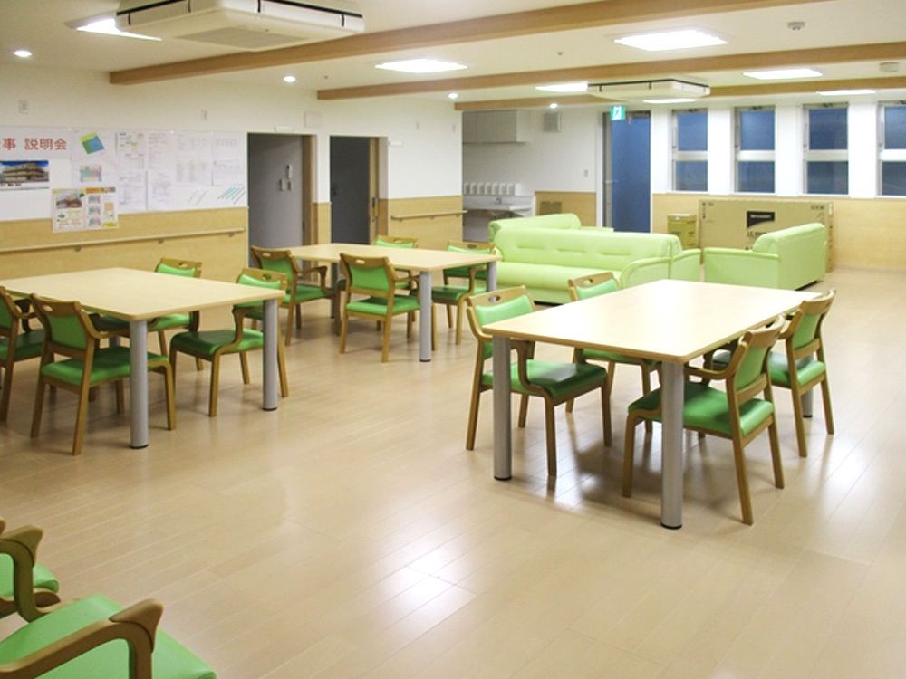 窓がたくさんあるリビングダイニング。木製のダイニングテーブルが複数置かれ、グリーンのソファもある。