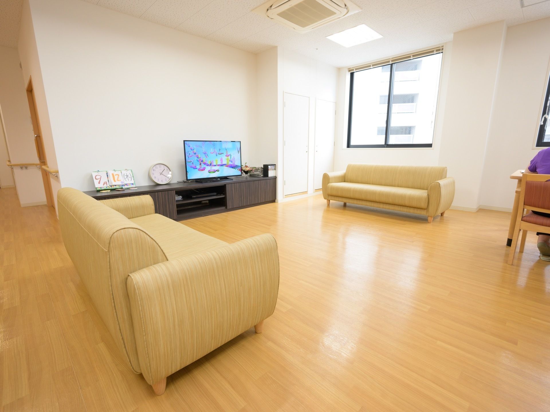 窓からは日の光が差し込み明るい。テレビ台にはテレビと小物がある。クリーム色のソファーが用意されいてる。