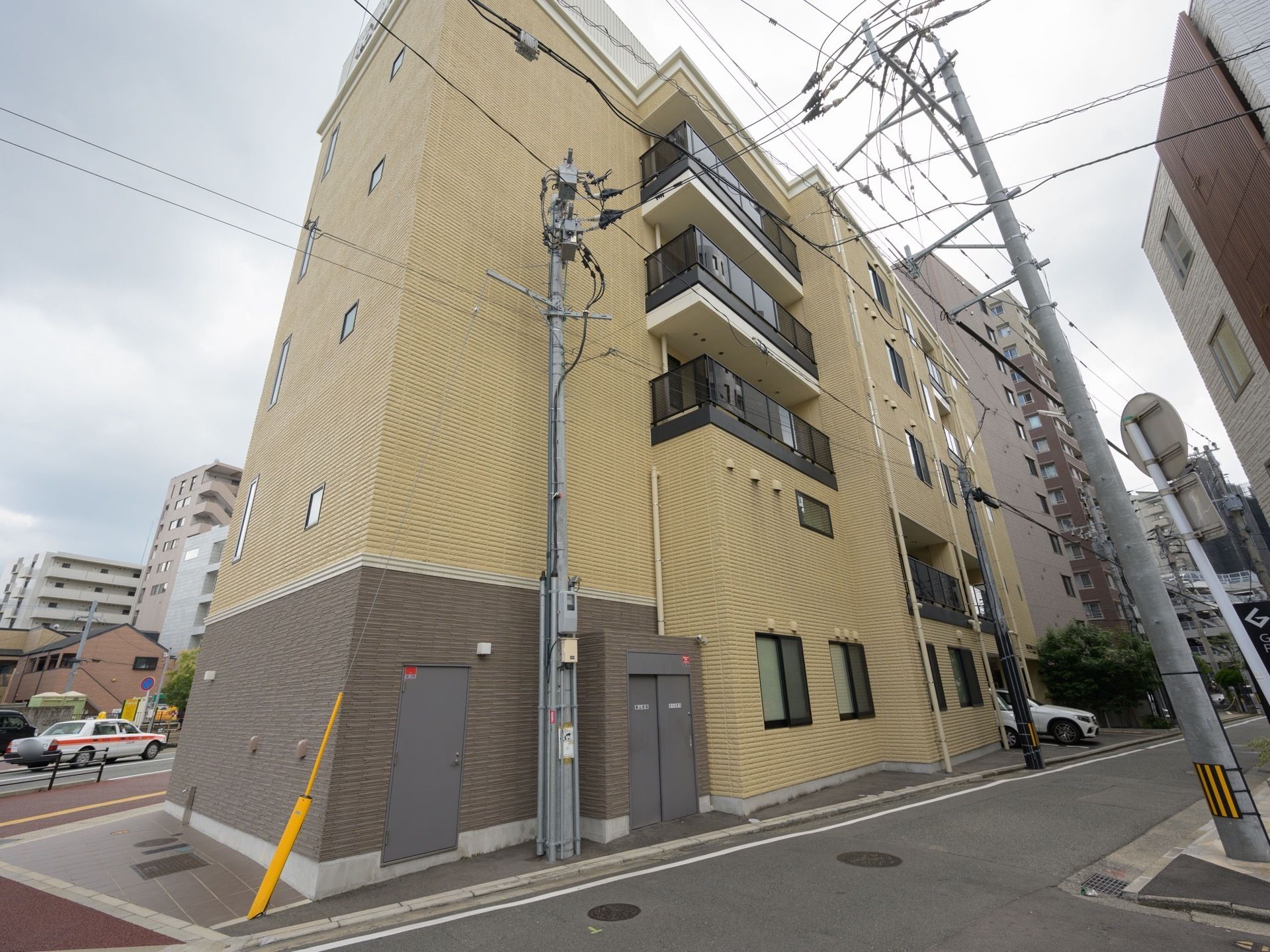 ベージュ調のマンション風の施設外観である。敷地内には駐車スペースが設けられており、車が1台停めれている。