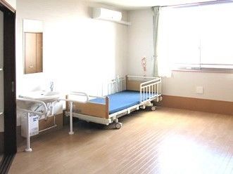 ベッドが置かれたフローリングの居室には、手すりが両サイドに設置された洗面所やエアコンもある。
