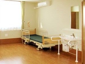 柵付きのベッドが置かれたフローリングの居室にはエアコンや洗面所が付いている。