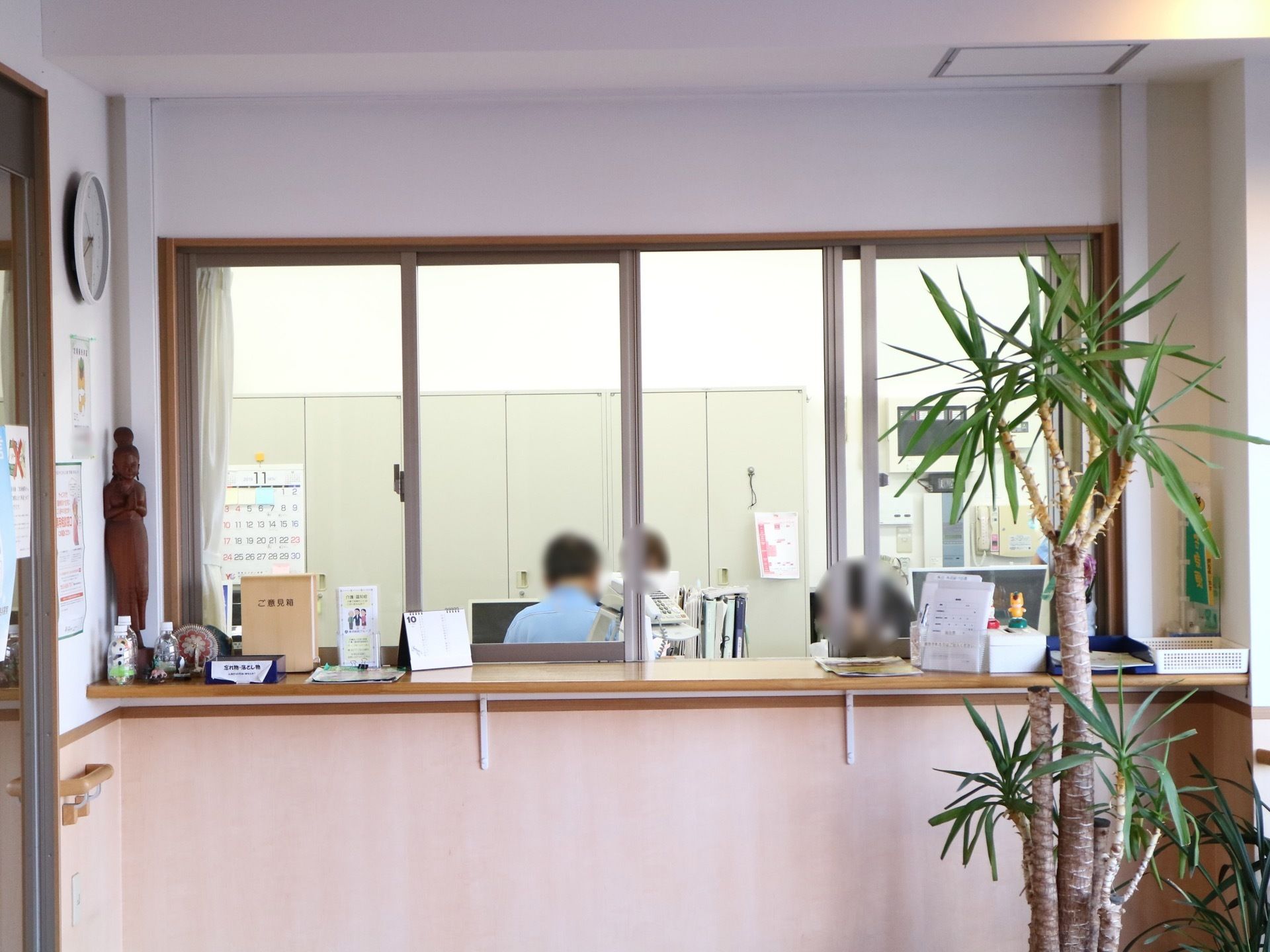 事務所の前に高窓があり、受付カウンターが設置されている。ご意見箱や受付簿、飾り物がカウンター上に置かれている。