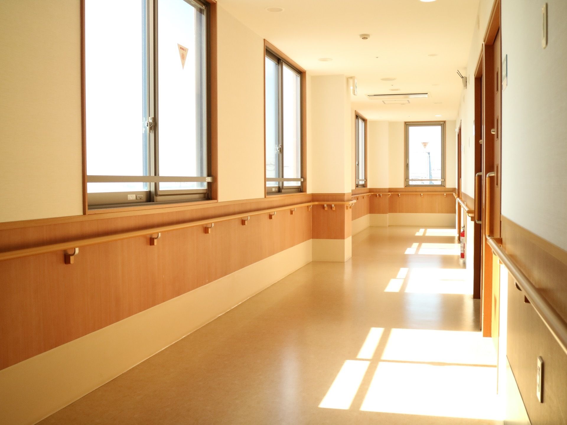 左側の窓から陽光が差し込んで床面に反射している。両側の壁には、腰高の位置に手すりが取り付けてある。右側に居室が並んでいる。