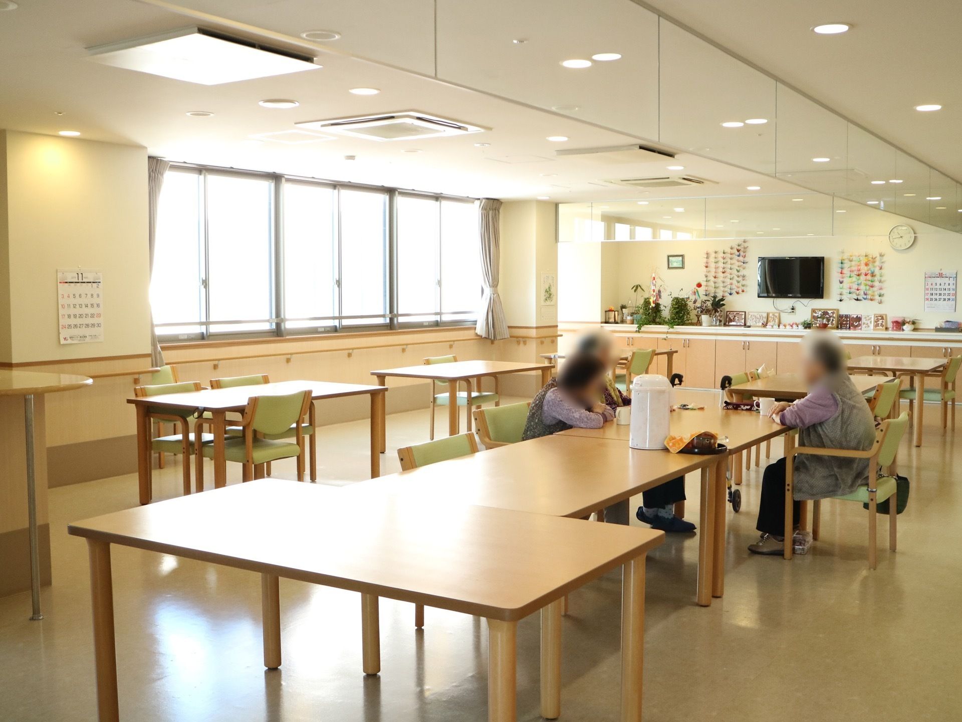 自然光も入る、明るい部屋である。テーブルに椅子がまばらに並べてある。ポットの置かれたテーブルを囲んで、入居者様数名が歓談中である。