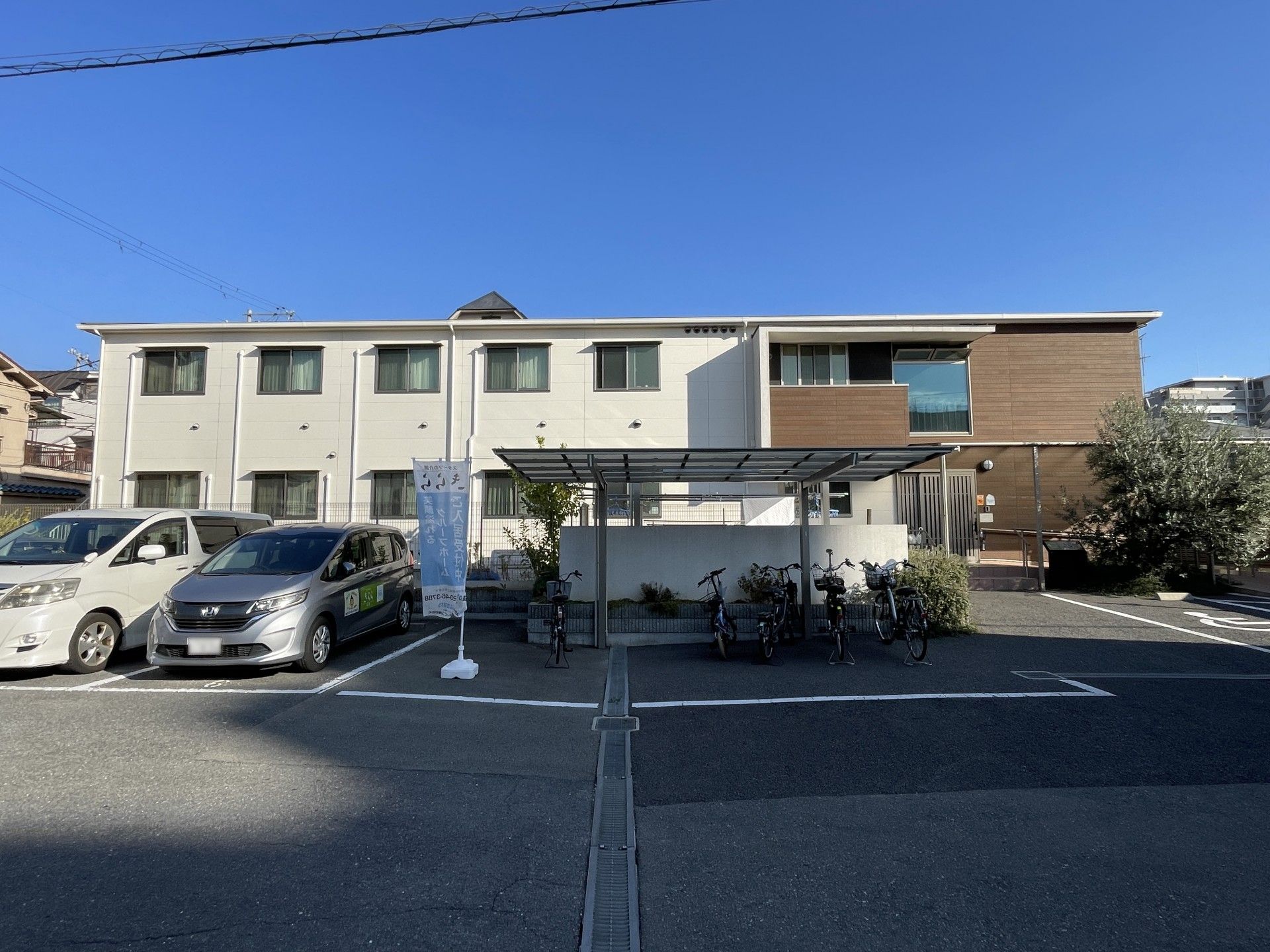 入り口にスロープがある、白と茶色のベージュの外壁の2階建てグループホーム