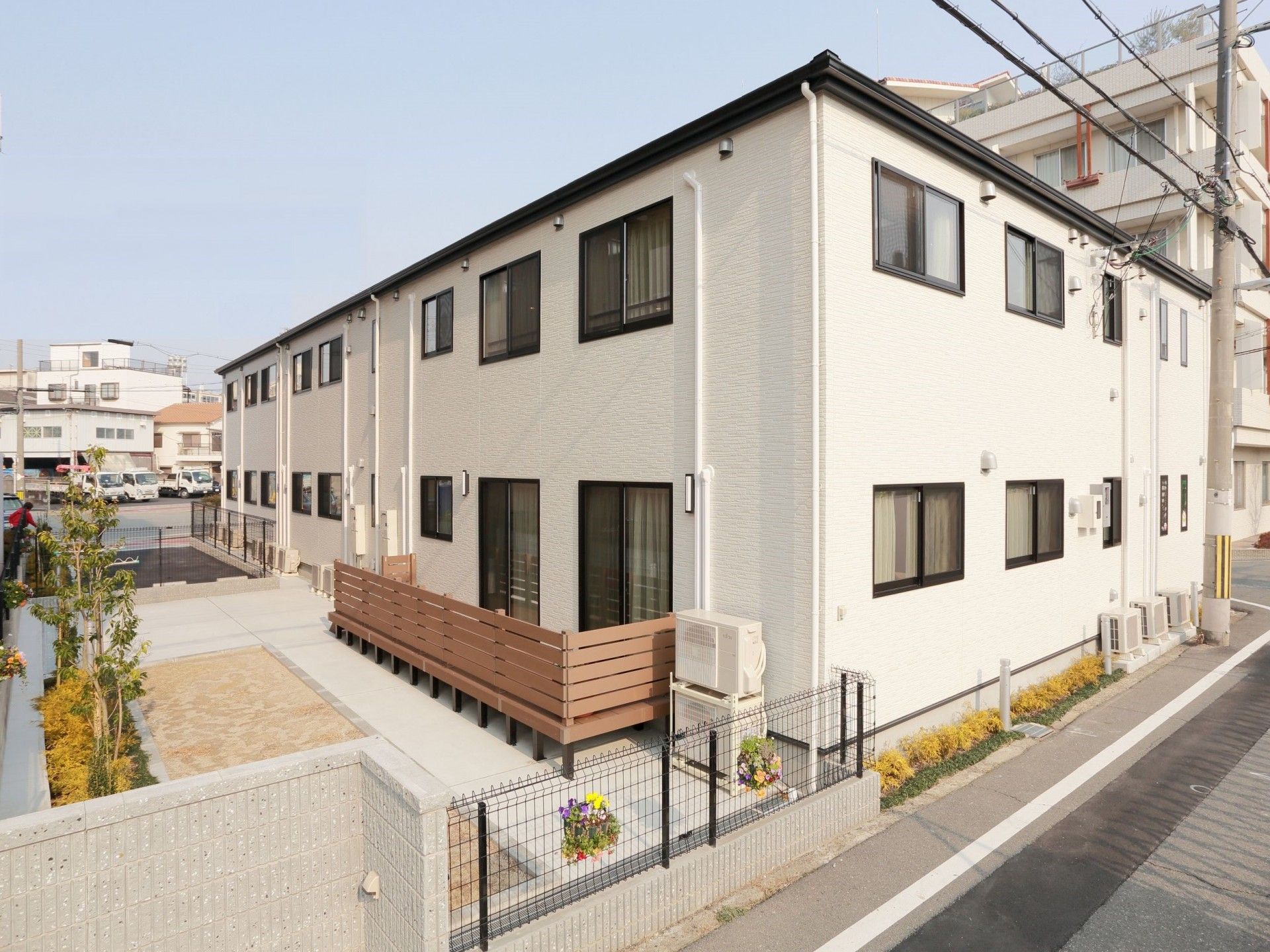 敷地内に花畑やウッドデッキがあるベージュの外壁の2階建てグループホーム