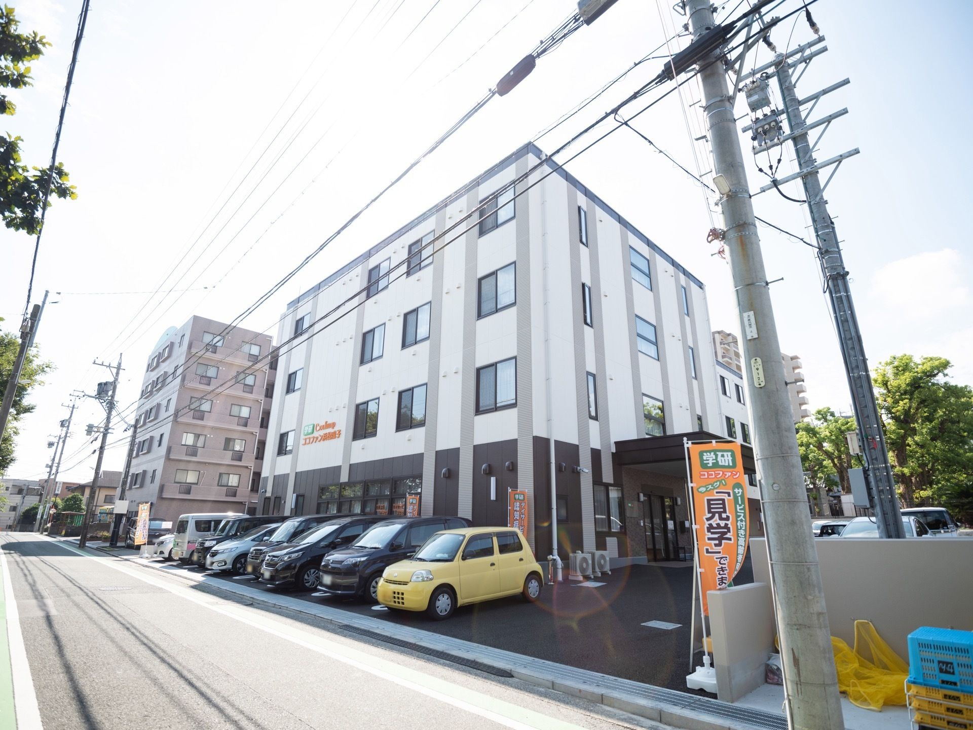 施設前の道路に面した側が駐車スペースとなっている。歩道との境や建物の前に複数枚の旗が立てられている。