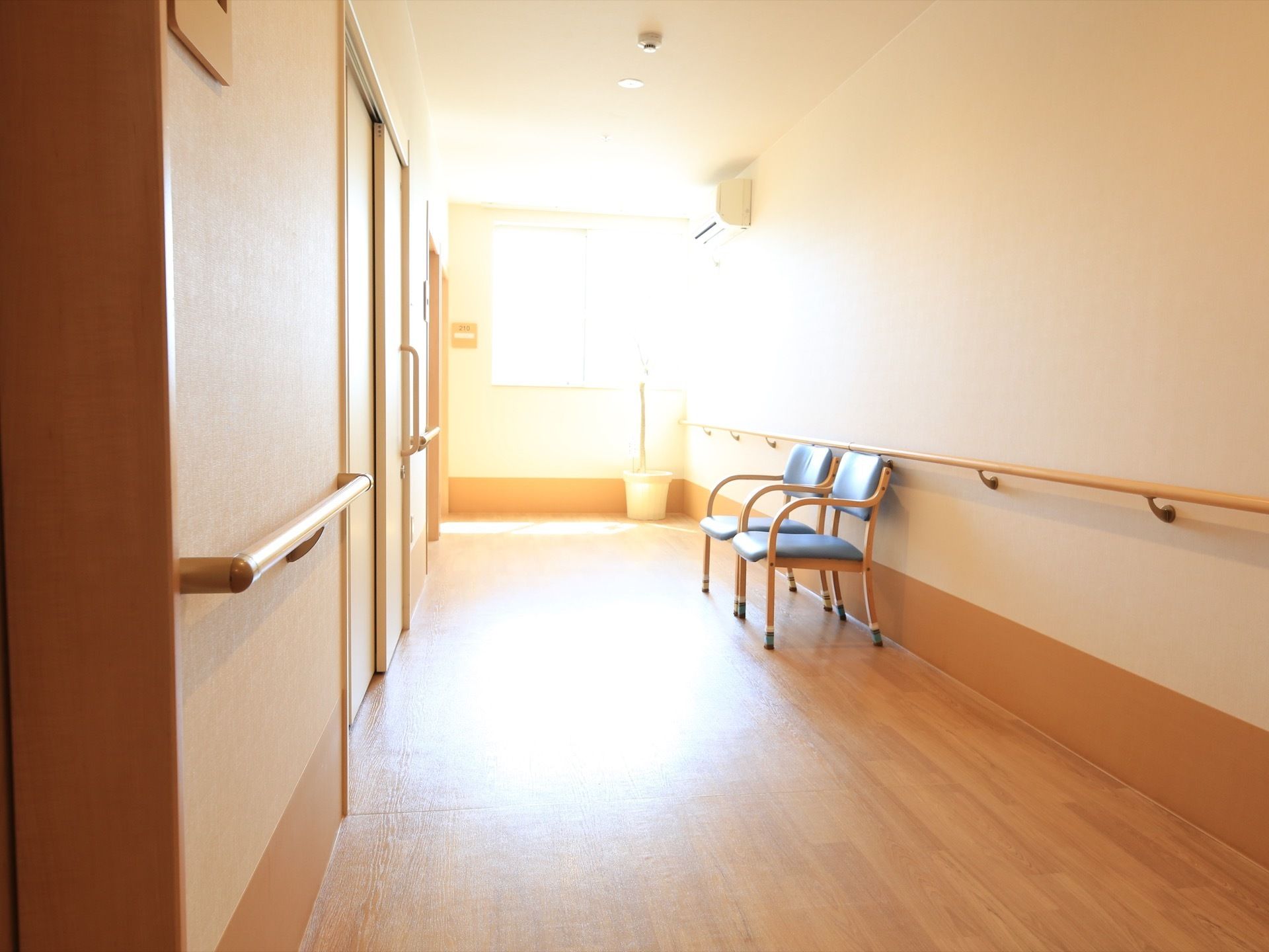 廊下はつきあたりの窓からの採光でとても明るい。壁際に、背もたれとひじ掛けがついた椅子が２脚並べて置かれている。