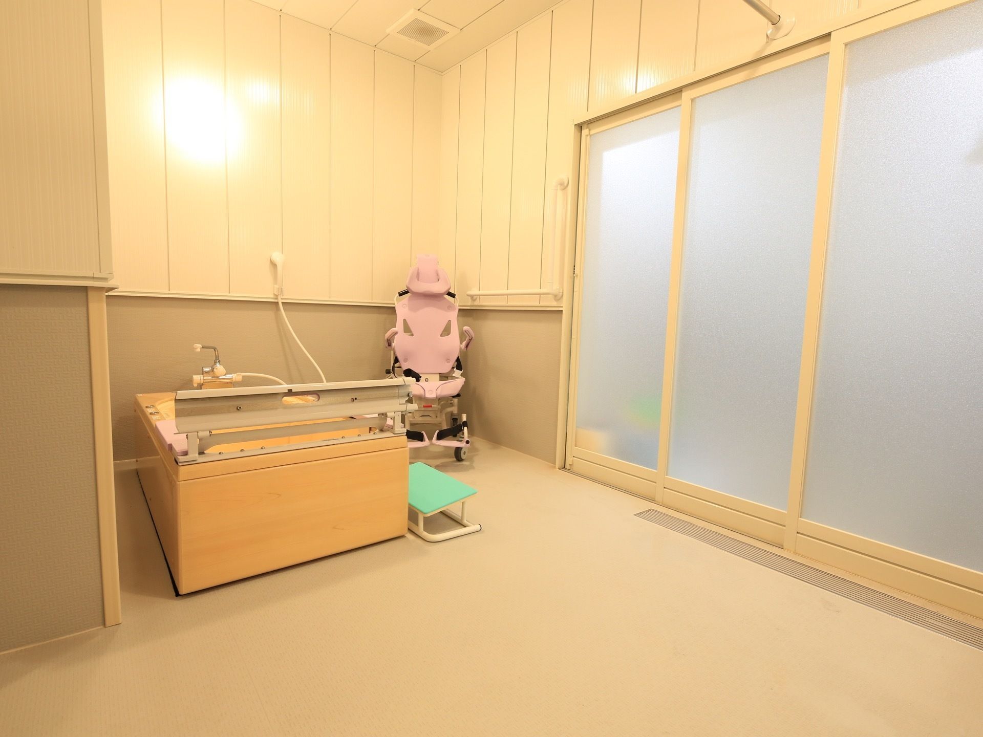 浴室に、大きな背もたれがついた可動式の椅子が置かれている。温かみのある色の浴槽で、その脇には踏み台がある。