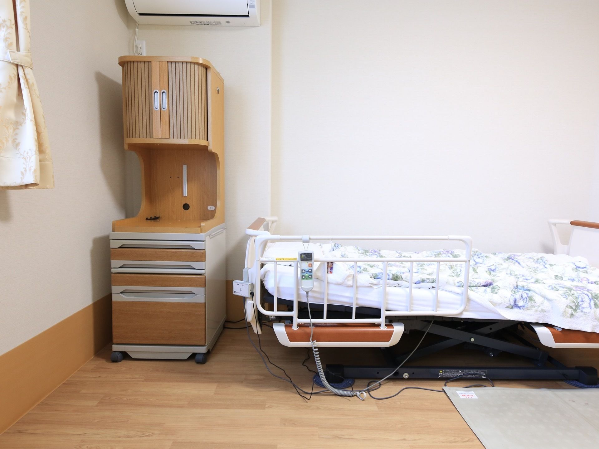 居室には、転落防止柵つきの介護ベッドが設置されている。ベッドの近くに、引き出しやじゃばらの扉がついた収納家具が置かれている。