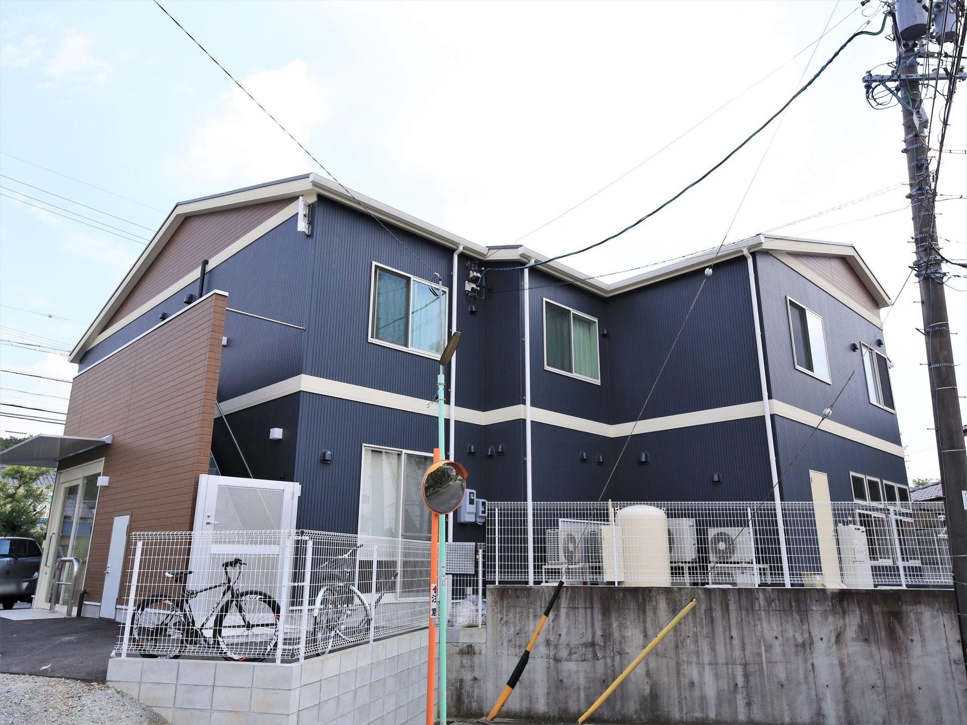 紺色と茶色を基調とした外壁の２階建ての施設である。敷地境界には、コンクリート塀や白いフェンスが設置されている。