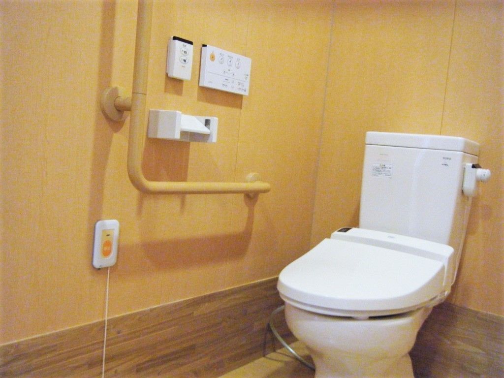 エル字型の手すりと緊急コールがついている施設内のトイレの写真