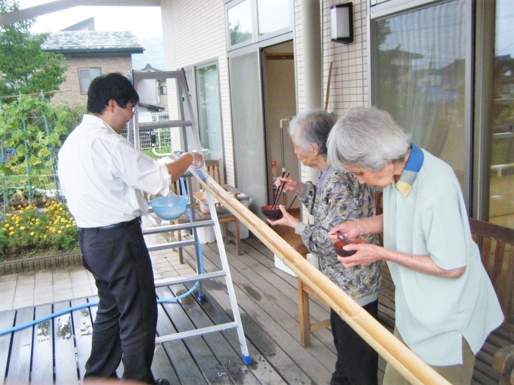 流しそうめんを楽しむ高齢者と施設のスタッフ。施設のテラス部分で楽しんでいる様子