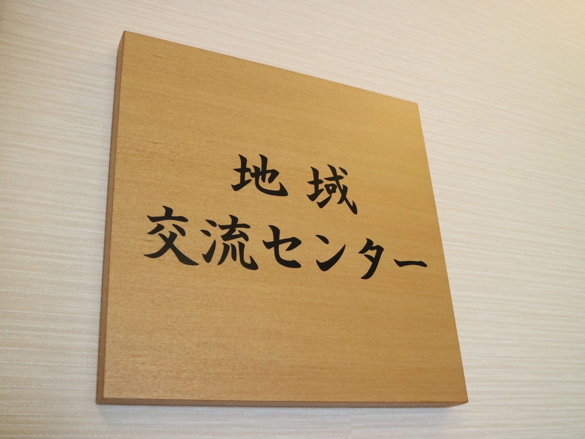 木のぬくもりが感じられるドアである。木製の四角いパネルには、黒い文字で地域交流センターの表示がされている。