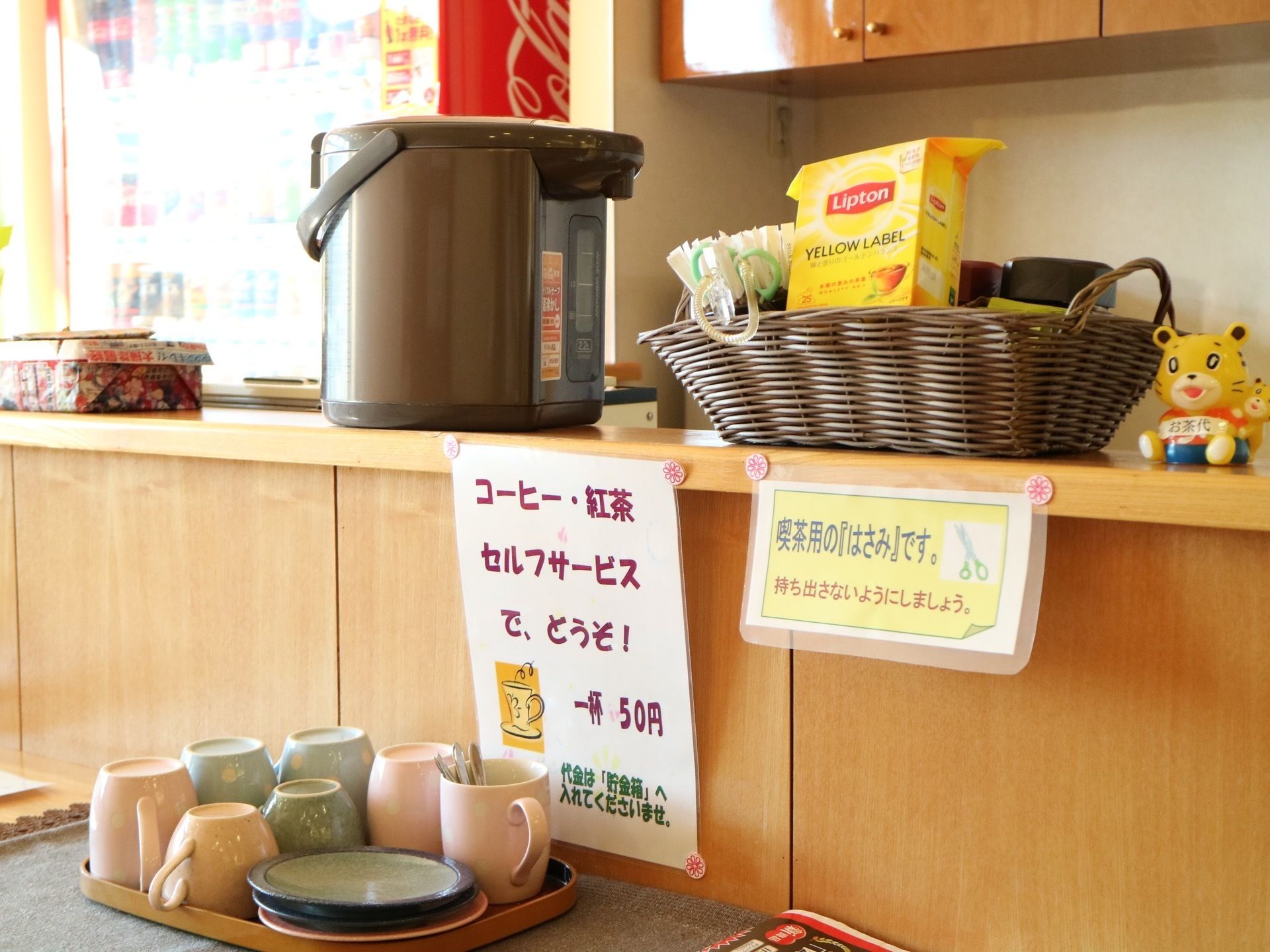 木製のカウンターに電子ポットやコップ、紅茶などが用意されている。奥には、自動販売機が設置されている。