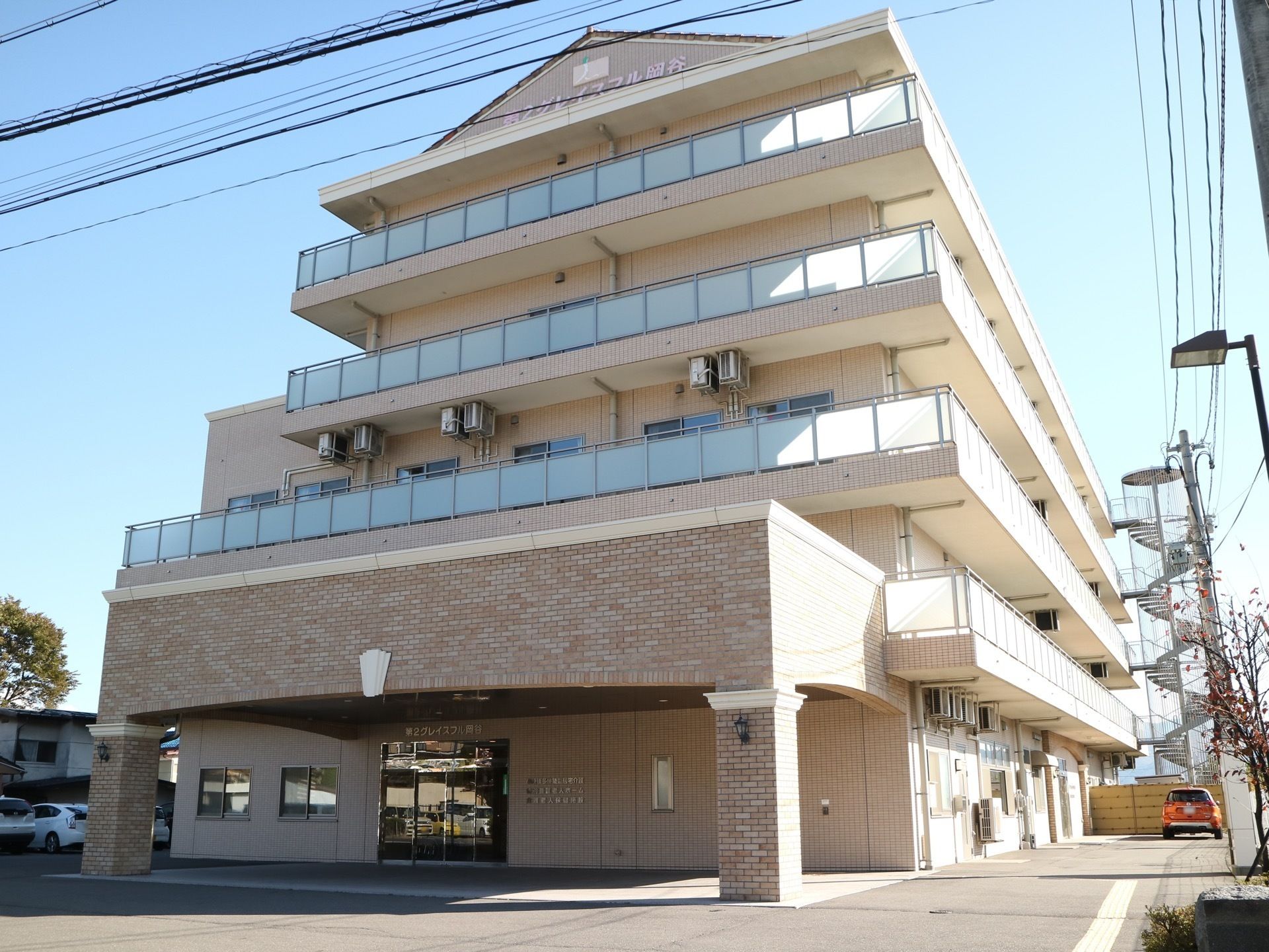 白を基調とした大きな５階建ての住まい。館内までのアプローチには段差がなく、玄関には屋根が設置されている。