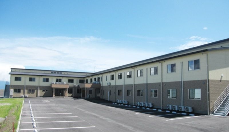 広い駐車場が付いた２階建ての建物はエル字型で日当たりのいい場所に建っている。
