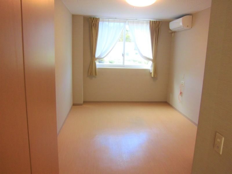 家具や家電がない居室はフラットフロアでエアコンと緊急通報装置があり、窓にはカーテンが付いている。