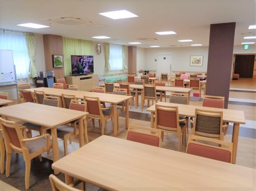 木製のダイニングテーブルが並び、左手にはテレビ、窓にはレースカーテンとカーテンが付けられ、壁には絵画が飾られている。