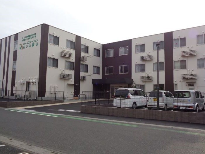 3階建ての建物。玄関には屋根が付き、外壁には住宅の名前が緑で書かれている。