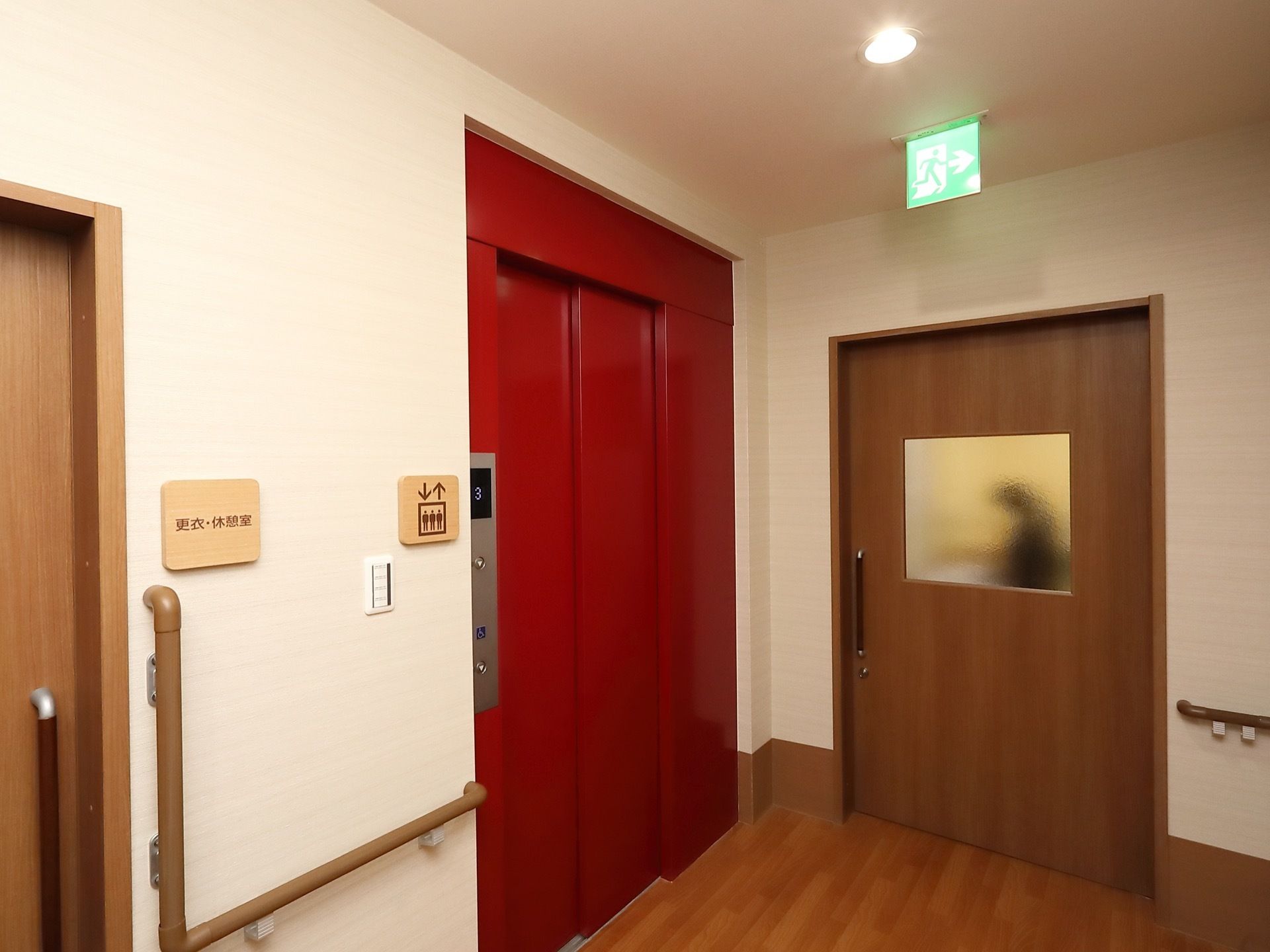 赤い扉のエレベーターが１基設置されている。ドアの横にはシルバーの操作パネルがあり、その横の壁にはエレベーターのマークが掲示されている。
