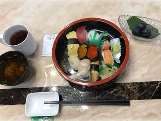 丸い寿司桶に盛られた一人分の握り寿司。ブドウやみそ汁もある。
