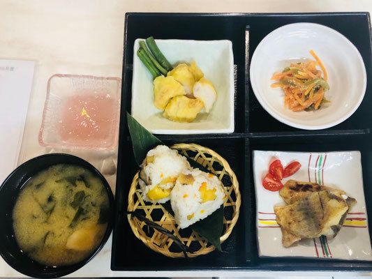 みそ汁の横には4つに仕切られた弁当箱風のお重があり、あえ物や揚げ物、煮物、おにぎりが盛られている。