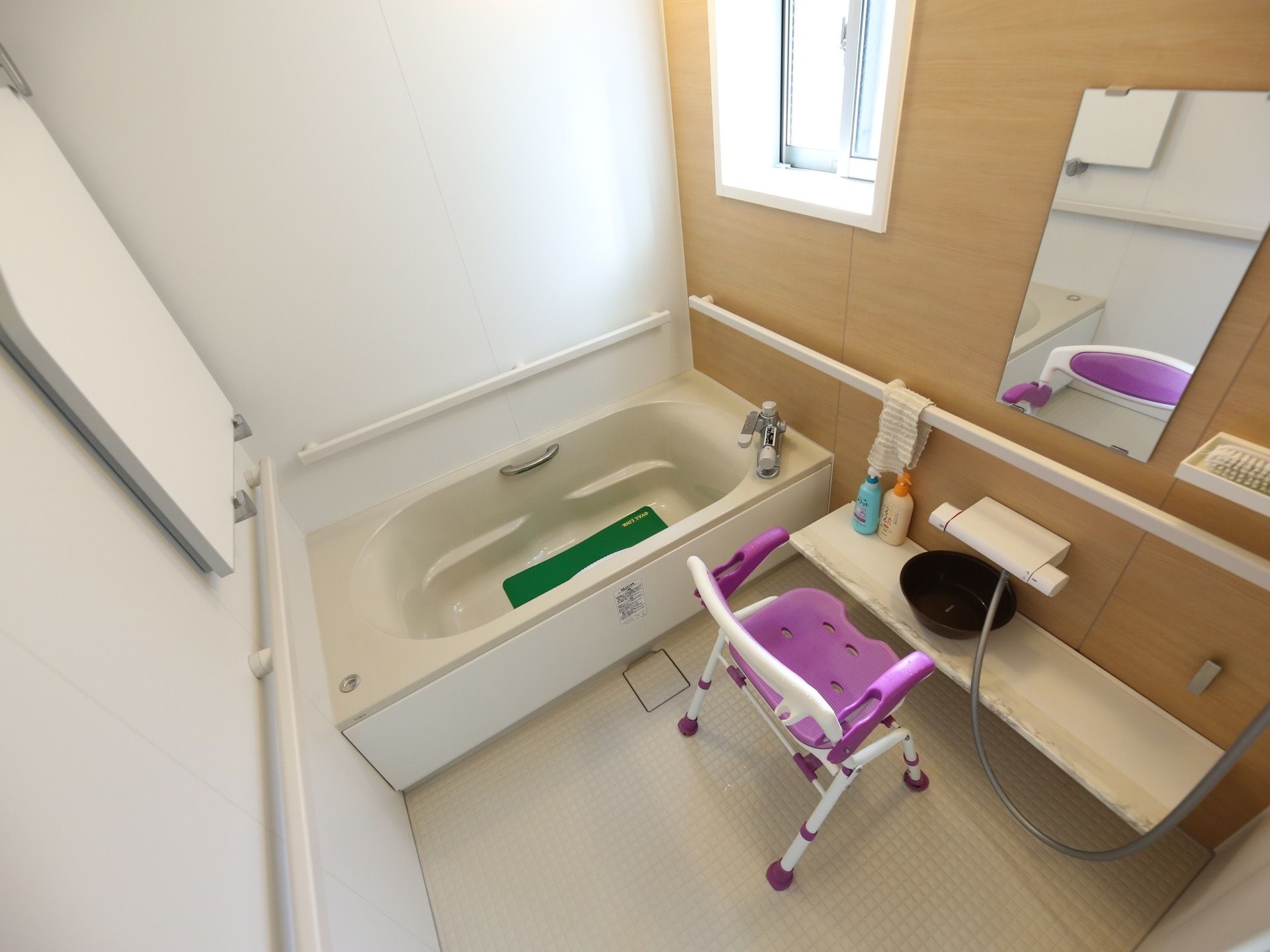 一部が木目調の壁になっている浴室がある。壁には四方に手すりが付いている。洗い場には鏡と入浴用の椅子が置かれている。