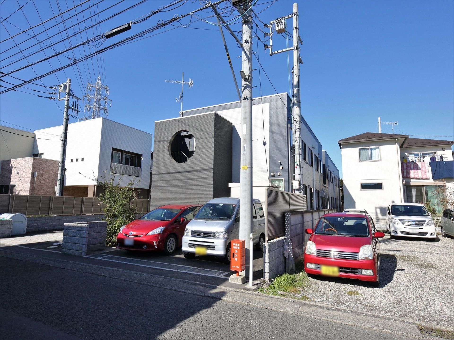 白とグレーを基調としたモダンなデザインの２階建ての建物がある。低い塀と植え込みで仕切られたとなりは駐車場になっている。