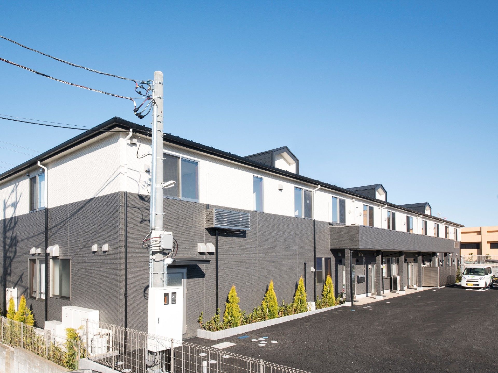周辺には木が植えられている2階建ての建物。広い駐車場があり、白い車が止まっている。