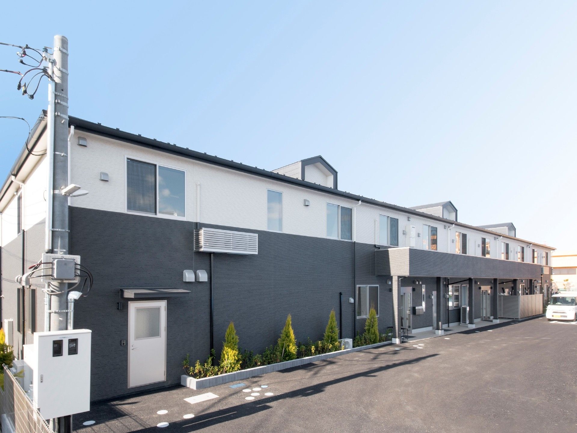 2階建ての建物。1階部分はダークグレー、2階部分は白で、広い駐車スペースや車寄せもある。
