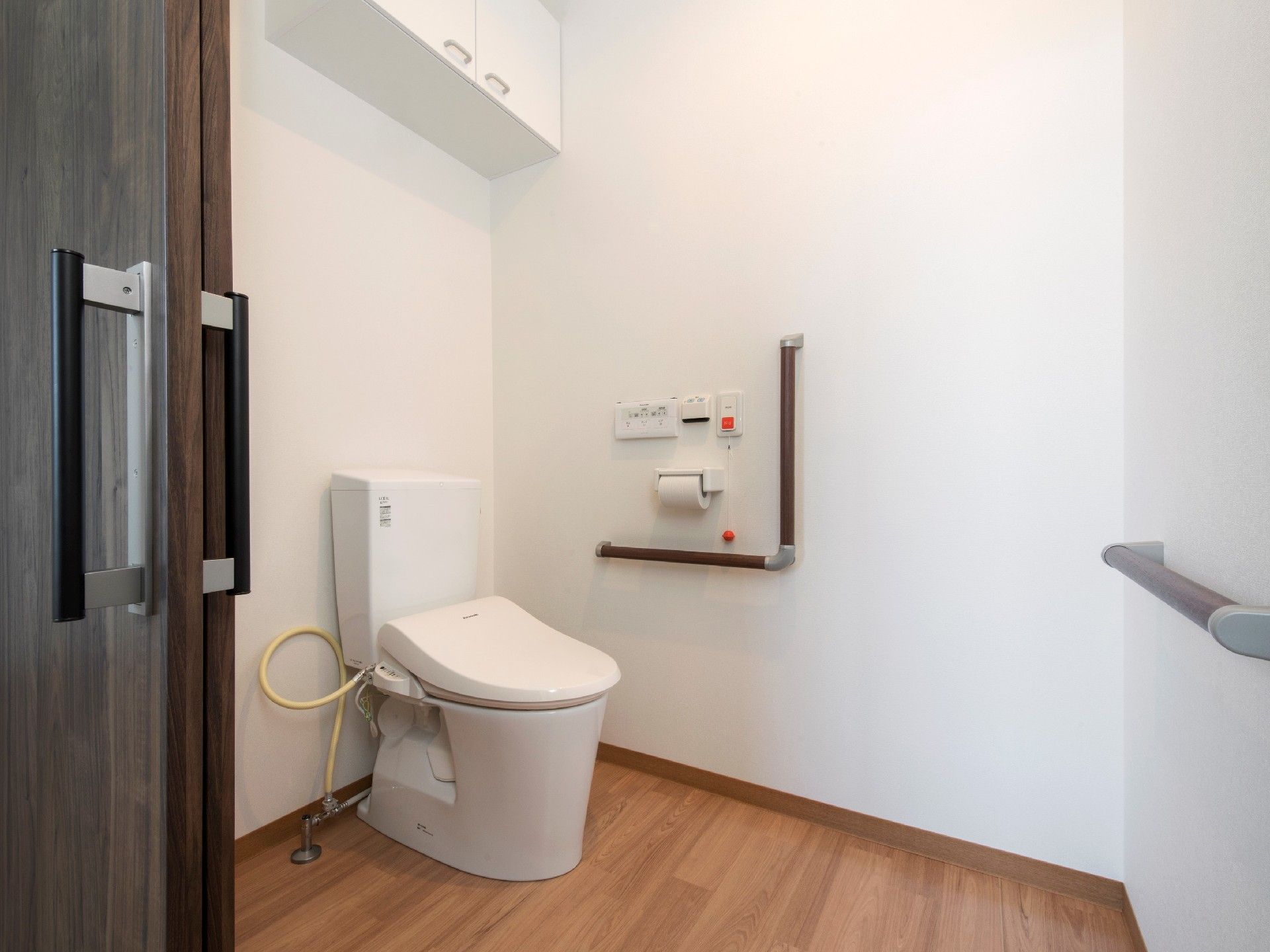 引き戸が付いたトイレは広く、壁にエル字型の手すりと呼び出しボタン、棚が付いている。