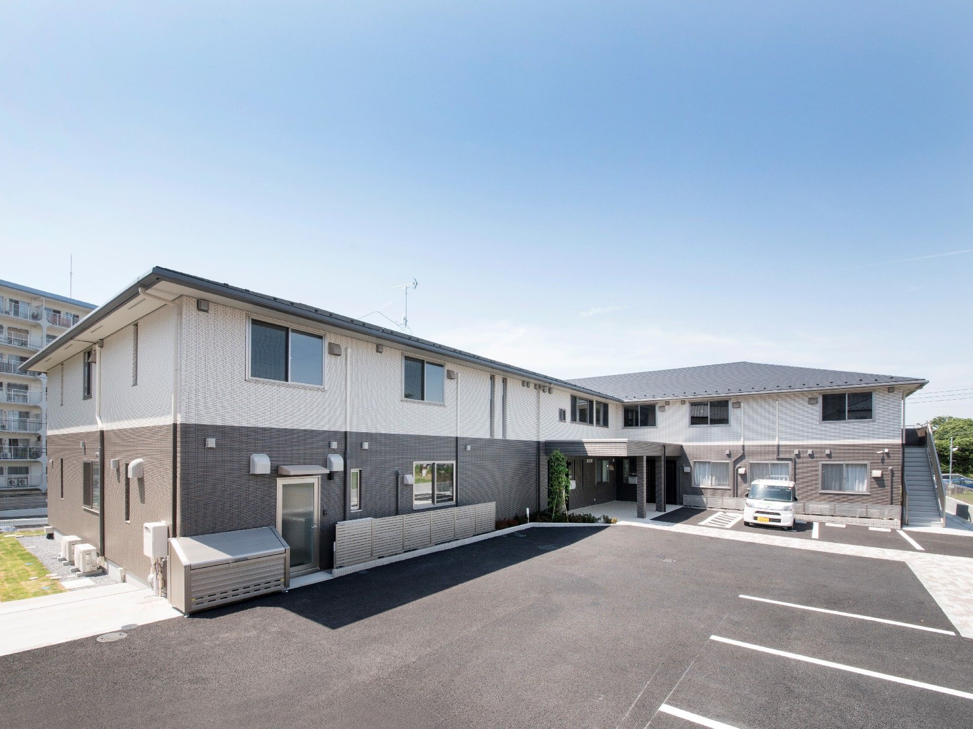 エル字型の建物は2階建てで1階部分はダークグレーでまとめられ、2階部分は白。青空が広がっている。