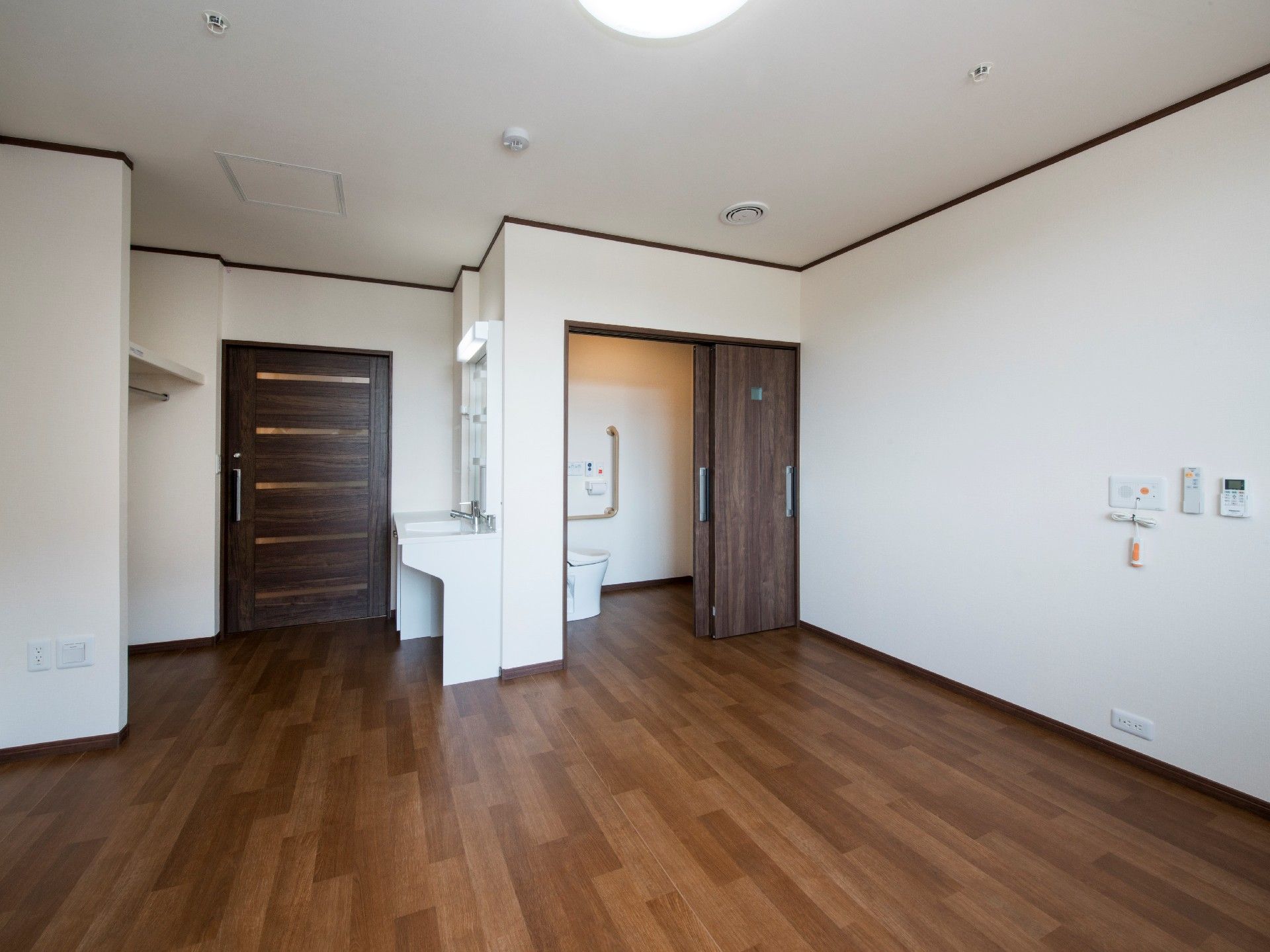 広々としたフローリングの居室。洗面所や収納スペース、照明があり、トイレもついている。