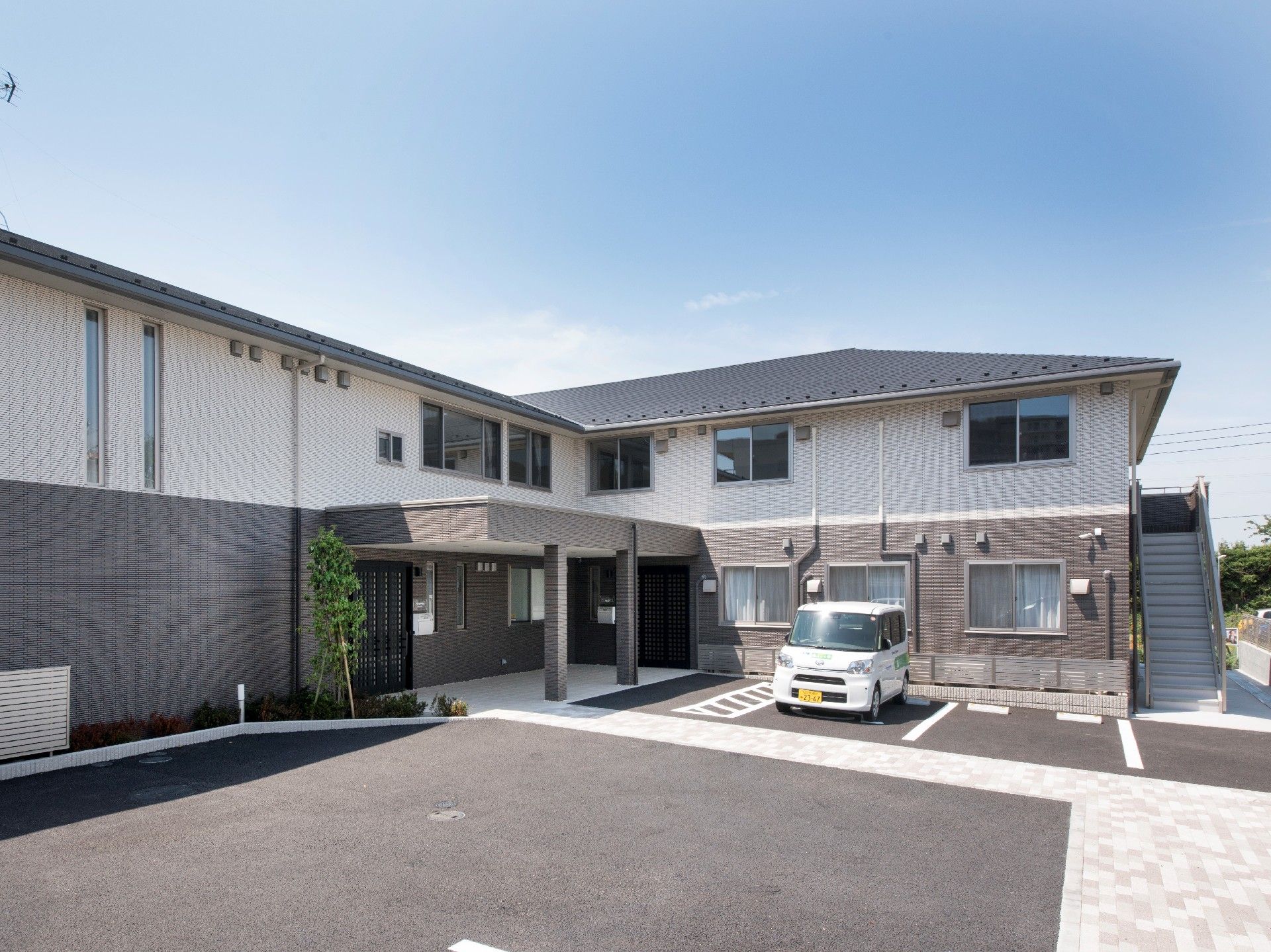 車寄せが付いた玄関がある2階建ての建物。周辺に緑が植えられている。